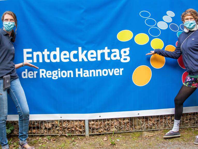 Zwei Damen zeigen auf ein Banner auf dem "Entdeckertag" steht